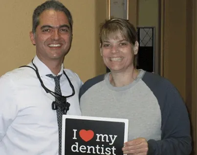 A patient holding an I love my dentist sign beside Dr. Okhovat.